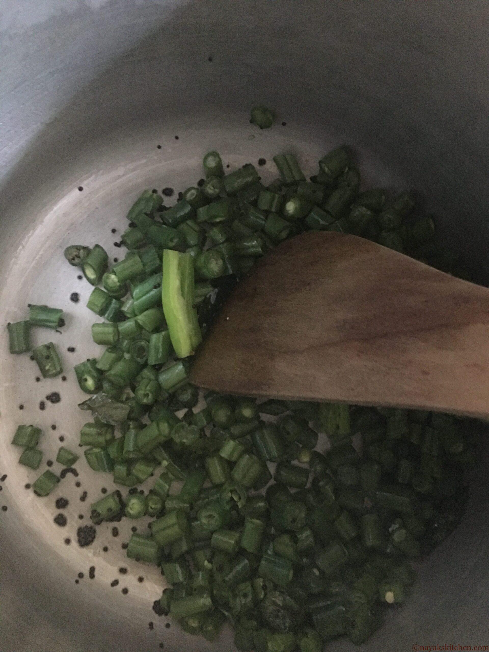 Stir frying french beans to prepare val papdichi bhaji