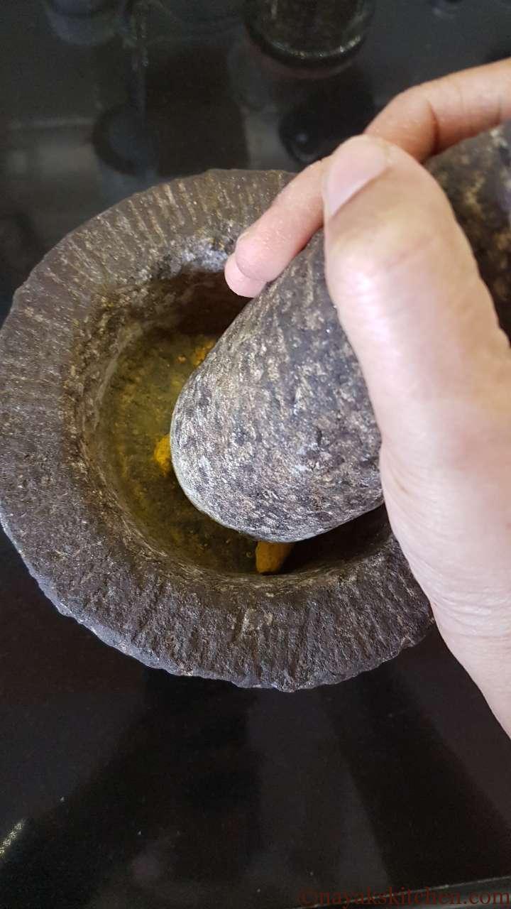 Crushing dried turmeric roots in a mortar and pestle.