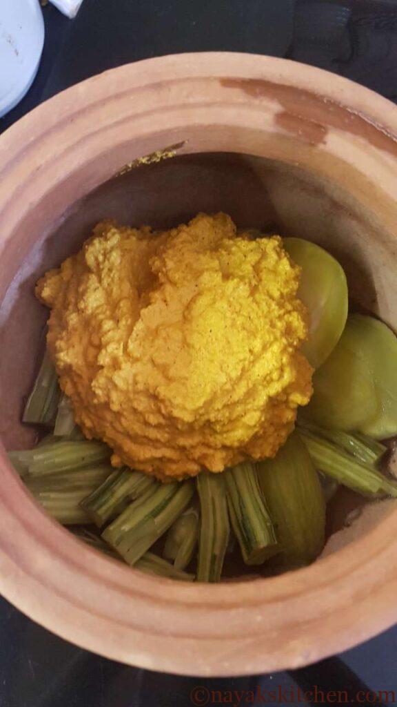 Adding ground paste to cooked drumsticks and raw mango